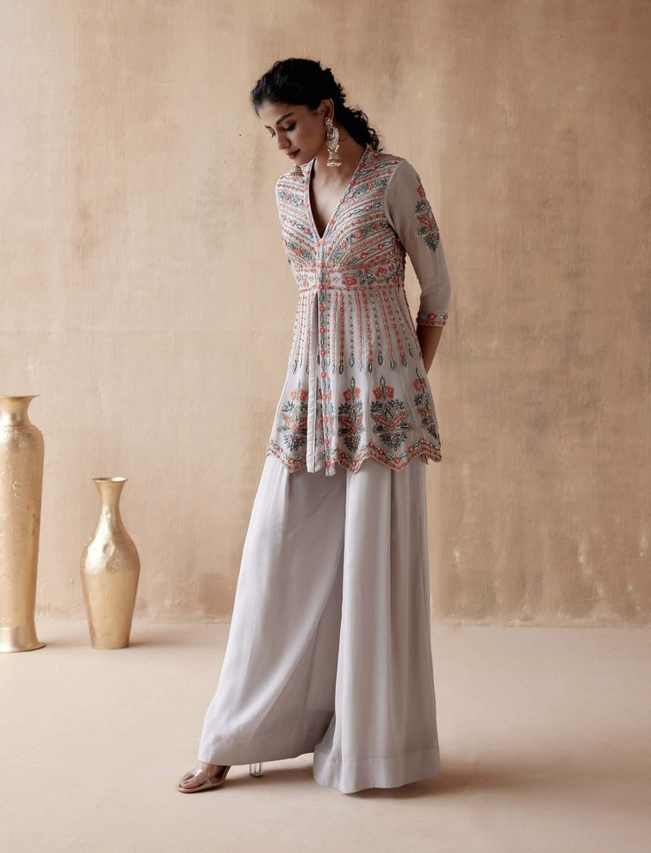 Editor's Note Introducing a graceful gray kurta adorned with intricate floral thread embroidery, elegantly highlighted with various embellishments. This captivating ensemble is paired with a stylish sharara, creating a sophisticated and elegant look perfect for special occasions or cultural events. The combination of the detailed embroidery and the classic silhouette of the sharara adds a touch of timeless beauty, making this outfit a tasteful choice for those who appreciate classic elegance wit Designer Floral Embroidered Floor-length Palazzo Set, Floor-length Floral Embroidered Palazzo Set For Diwali, Straight Kurta Pant Set For Navratri Wedding, Semi-stitched Floral Embroidered Floor-length Palazzo Set, Wedding Pant Set With Straight Kurta For Navratri, Elegant Floral Embroidered Pant Set For Diwali, Festive Floor-length Floral Embroidered Sharara, Gray Long Sleeve Wedding Set, Floral Embroidered Floor-length Sharara For Eid