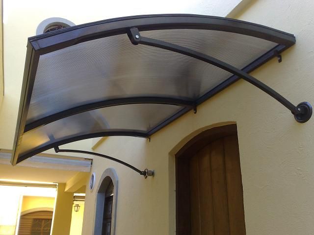 an outside view of a house with a door and window in the background, there is a metal awning over the doorway