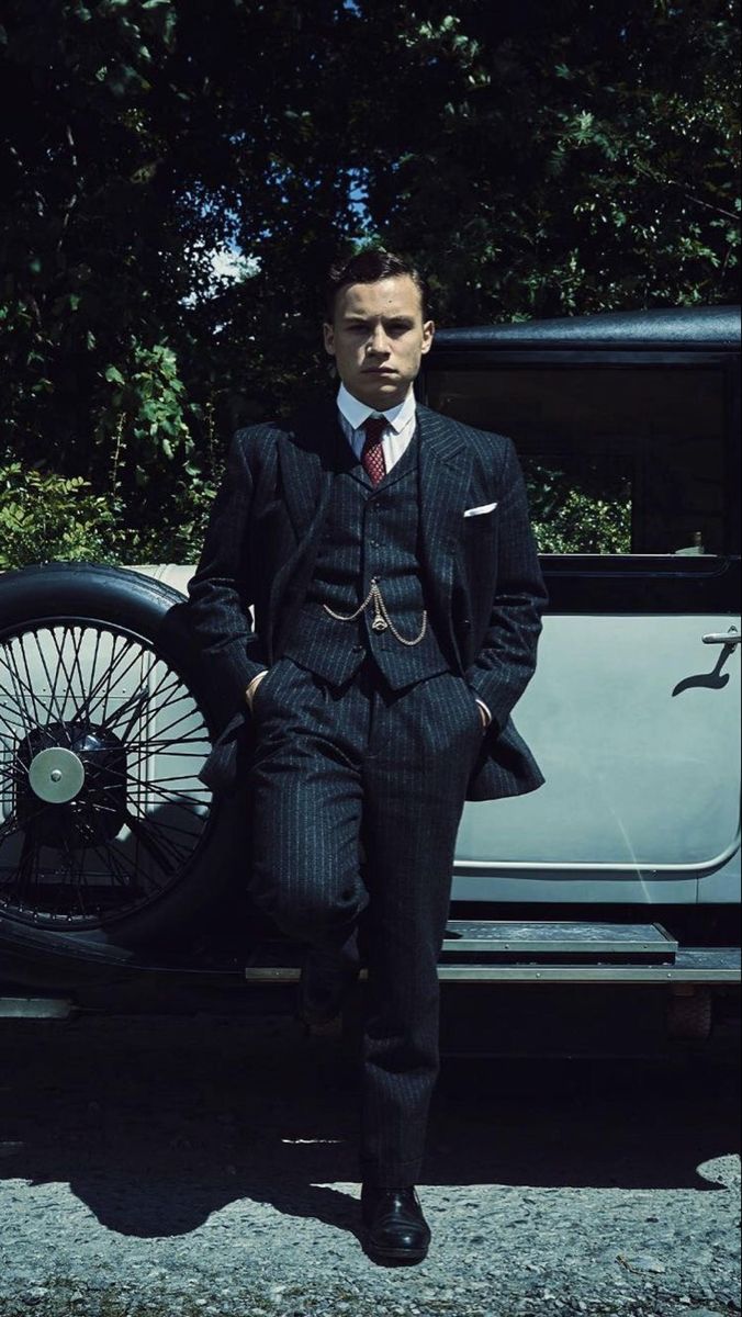 a man in a suit standing next to an old car