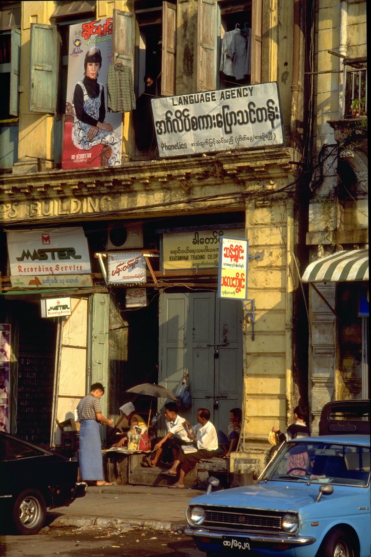 an old building with people sitting on the windows and cars parked in front of it