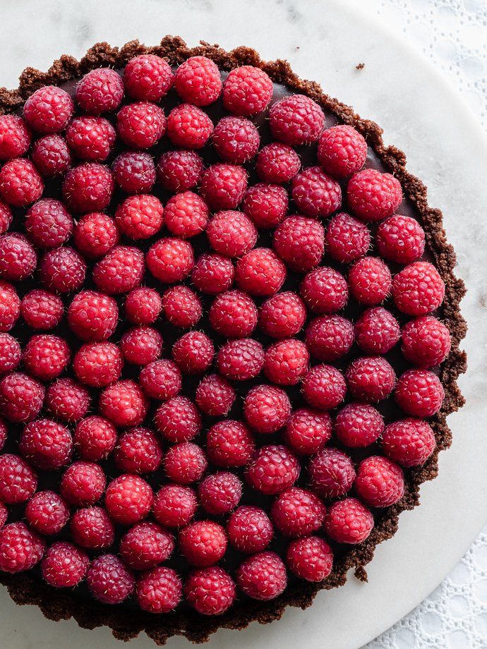 a chocolate tart topped with raspberries on top of a white platter