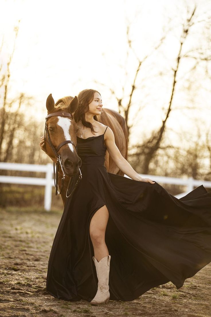 a woman in a long black dress is walking with a horse and posing for the camera