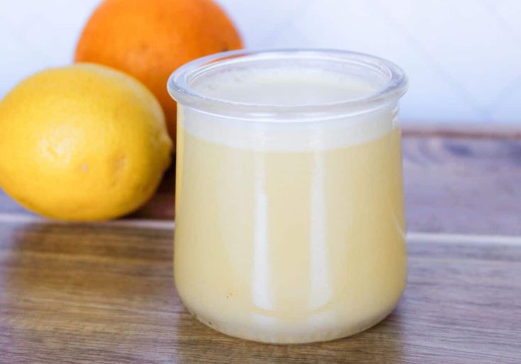 a glass jar filled with liquid next to two oranges