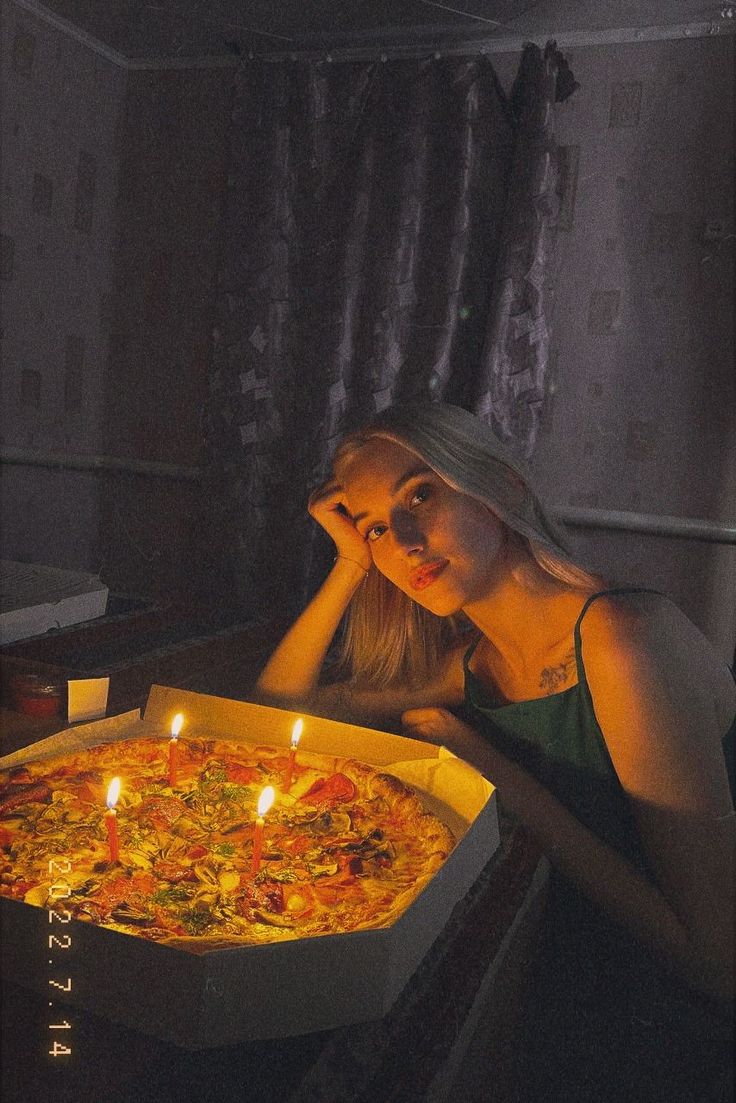 a woman sitting in front of a pizza with candles on it