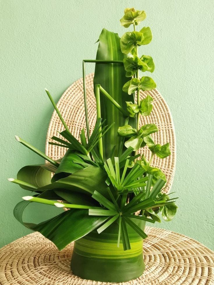 a green vase filled with plants on top of a wicker table