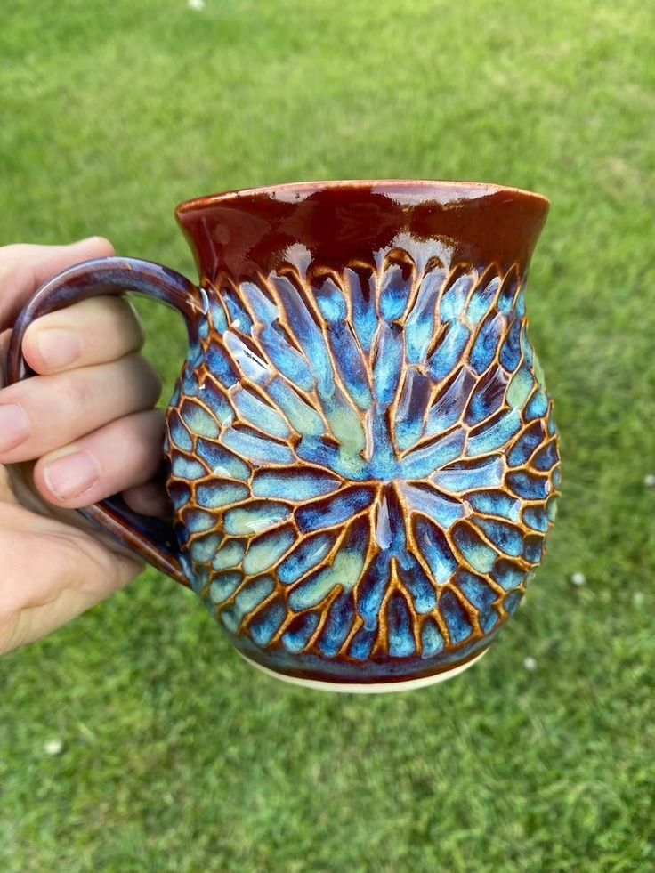 a hand holding a blue and brown vase on top of green grass in the sun