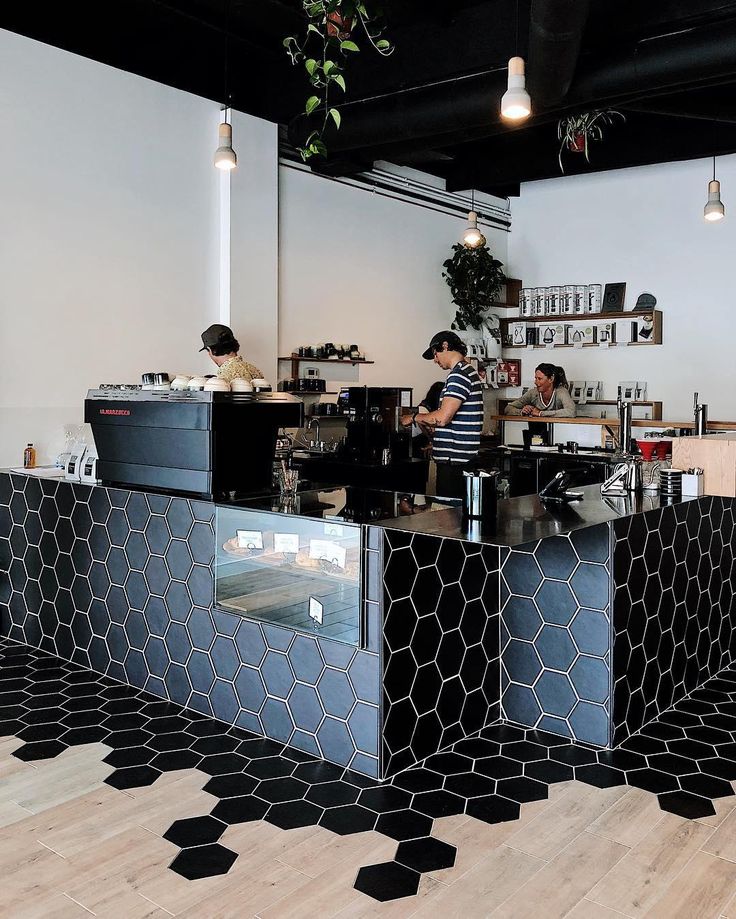 the interior of a coffee shop with black and white tiles on the floor, two men working behind the counter