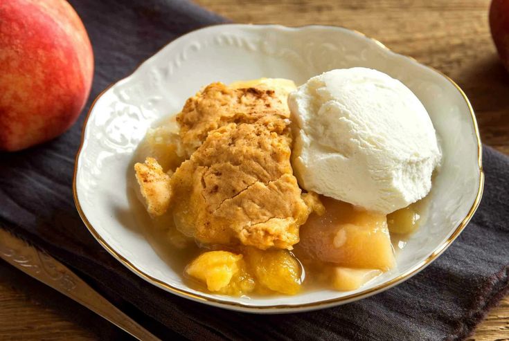 an apple cobbler with ice cream and two pieces of fruit on the table next to it