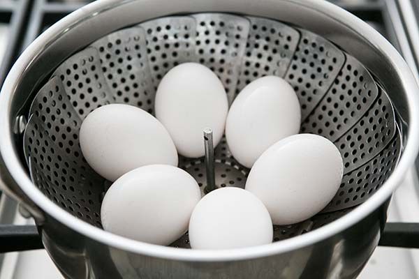 six white eggs in a colander on the stove