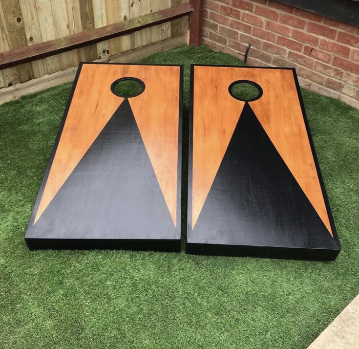 two black and orange triangle shaped cornhole boards on green grass in front of a brick wall