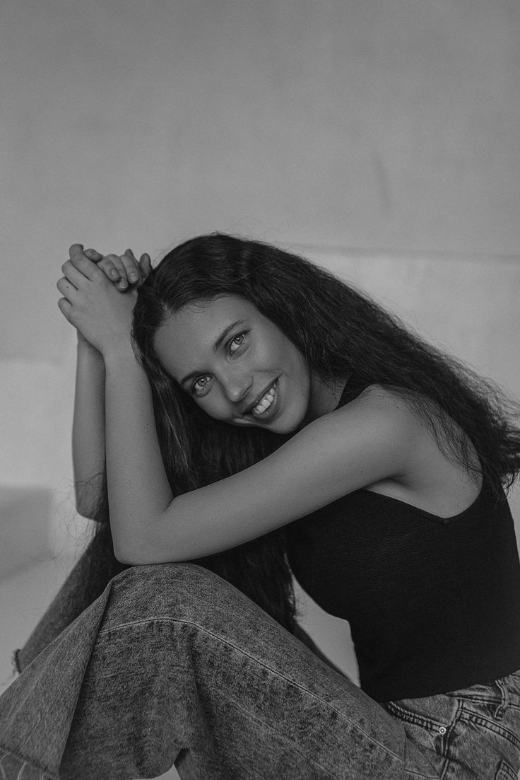 a black and white photo of a young woman sitting on the floor with her arms behind her head