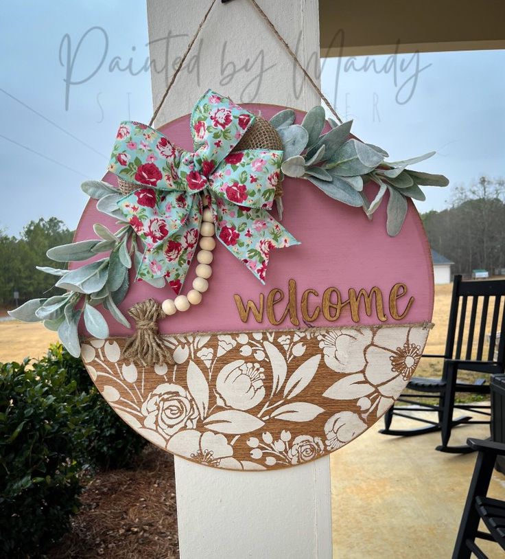 a welcome sign hanging from the side of a white building with flowers and leaves on it