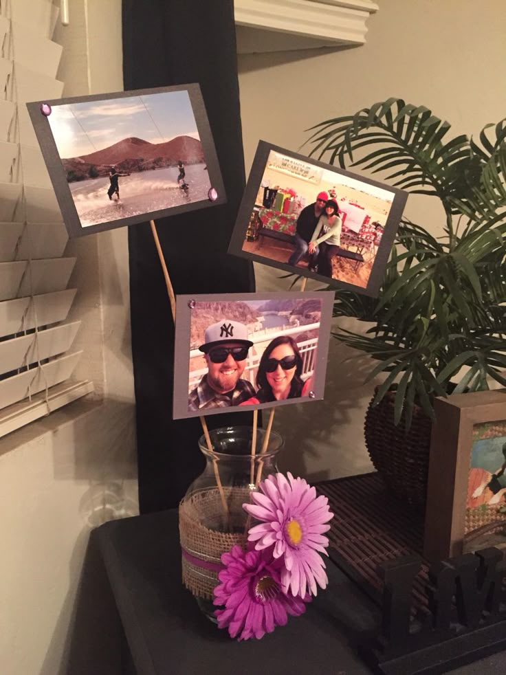 there is a vase with flowers and pictures on the table next to some photos in frames