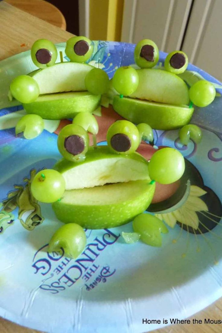 there is a paper plate that has some green frogs on it with apples in front of them