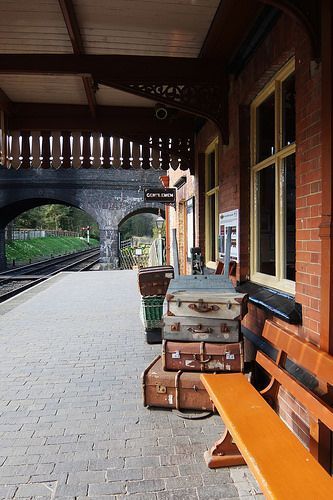 several pieces of luggage sitting on the side of a train station platform next to a bench