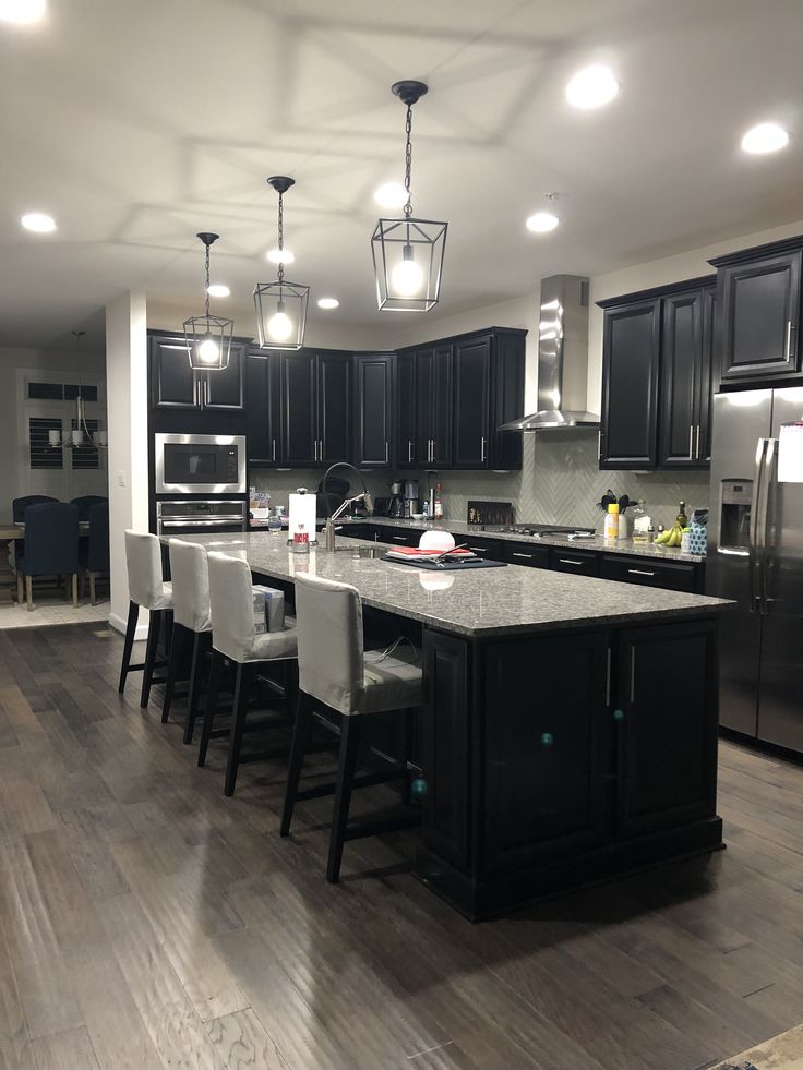 a large kitchen with black cabinets and an island in front of the stove top oven