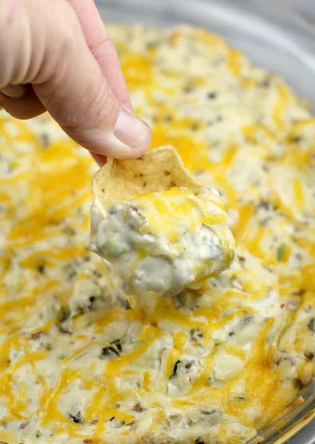 a hand dipping a tortilla chip into a glass bowl filled with melted cheese