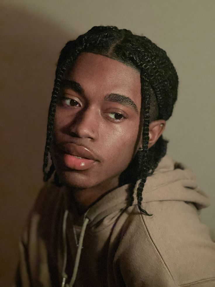 a young man with dreadlocks on his head looking at the camera while wearing a hoodie