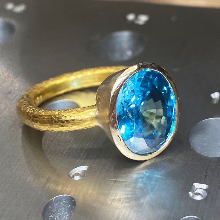 One-of-a-kind, hand-crafted ring centering 10.20 carat oval shape, fine gem quality vivid color Blue Zircon set in 18karat yellow gold bezel and 22karat yellow gold hammered setting. Size 7, can be sized upon request. Zircon might be one of the most under-appreciated colored gemstones and please do not confuse it with cubic zirconia, or CZ, an artificial product from the mid-1970s. Zircon found in Australia is the oldest mineral on earth: 4.4 billion years old. In the Middle Ages, this gem was t Unique Oval Yellow Gold Topaz Ring, Gold Blue Topaz Ring With Bezel Setting, Gold Oval Topaz Ring With Bezel Setting, Oval Yellow Gold Topaz Ring With Bezel Setting, Handmade Gold Topaz Ring In Oval Shape, Handmade Gold Topaz Ring With Oval Shape, Royal Blue Sapphire Ring, Fine Jewelry Rings, Pink Opal Ring