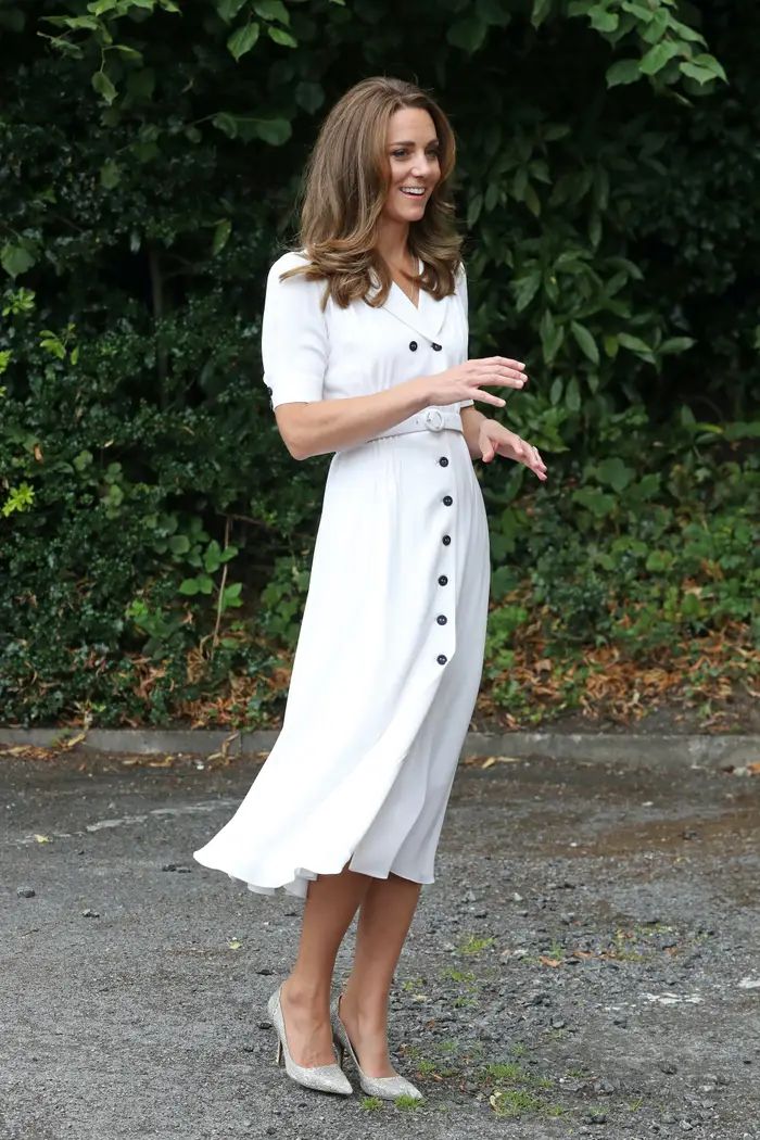 the first lady is wearing a white dress with buttons on it and she is standing in front of some bushes