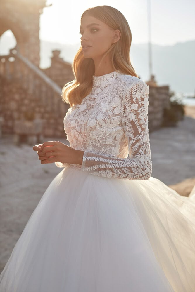 a woman in a white wedding dress standing on the beach with her hand on her hip