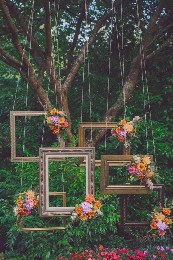 four frames hanging from a tree with flowers and greenery in the foreground, on which is an arrangement of pink and orange flowers