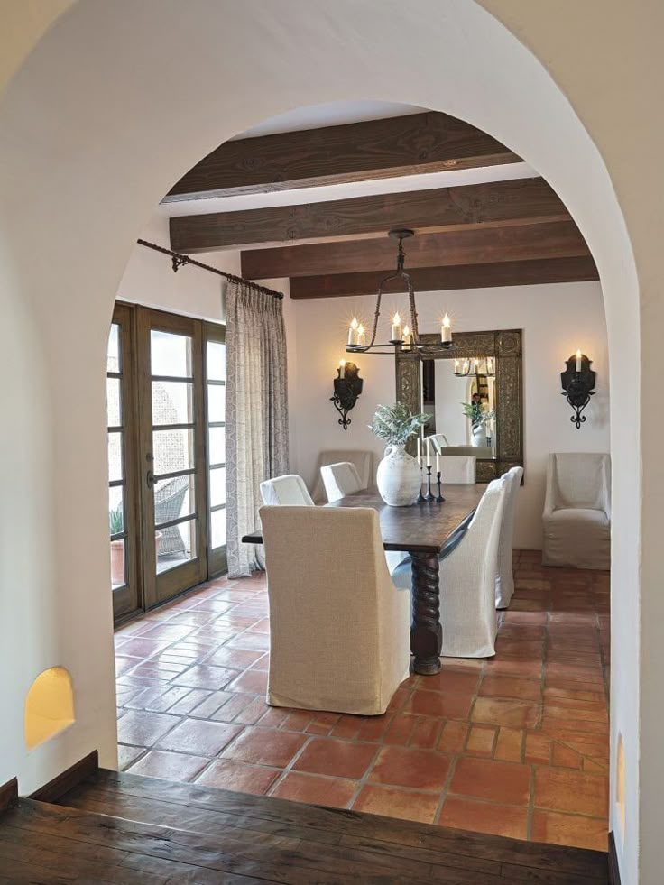 a dining room table with white chairs and an archway leading to the living room area