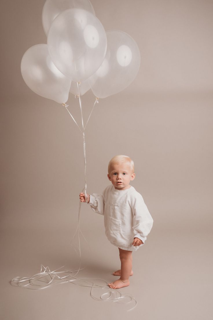 a baby is holding some white balloons