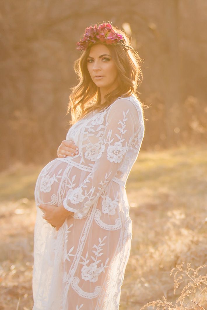 a pregnant woman wearing a white lace dress in a field with flowers on her head