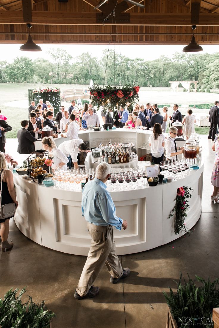 A white round bar set up in an open air patio, surrounded by happy guests. Cocktail Set Up Wedding, Cocktail Bar Wedding Receptions, Bar Decorations Party, Bar Design For Wedding, Cocktail Party Setup Ideas, Rooftop Cocktail Hour Wedding, Bars For Wedding Reception, Cocktail Hour Wedding Set Up, Cocktail Wedding Furniture