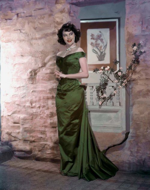 an old fashion photo of a woman in a green dress standing next to a brick wall