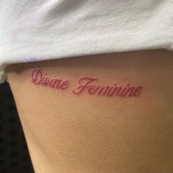 a woman's thigh with the word divine feminine written in cursive font