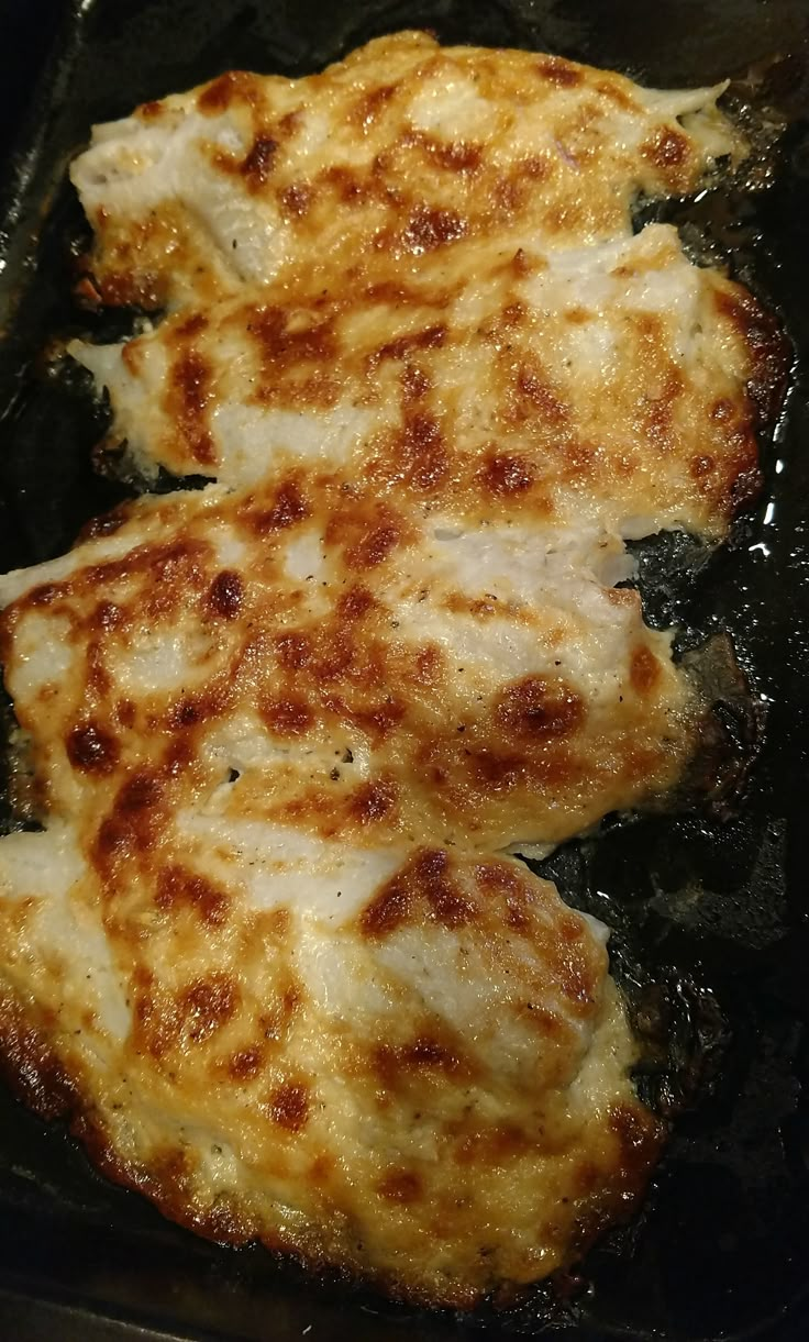 two pieces of chicken cooking in a pan on the stove top, with oil coming from it