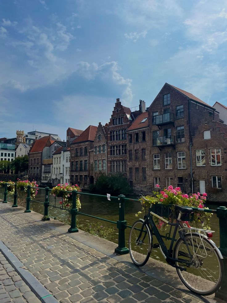 a bicycle parked on the side of a bridge next to flowers and buildings in the background