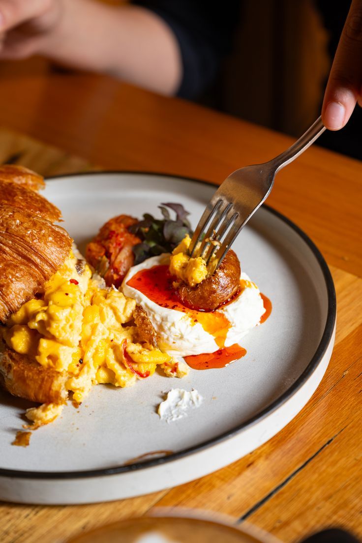 a person is holding a fork over a plate with eggs and croissants