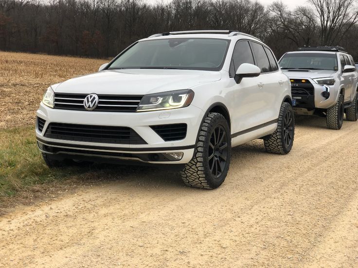 two white volkswagen suvs driving down a dirt road