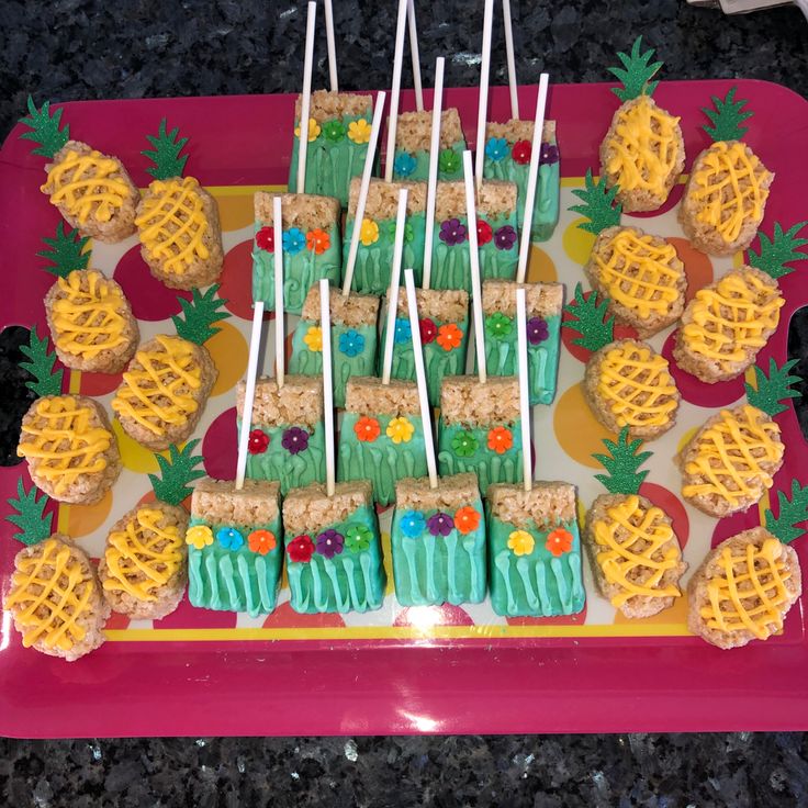 there are many cupcakes on the tray with pineapples and flowers in them