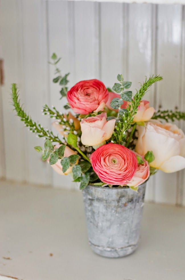 a bouquet of flowers in a bucket on a table next to a white wooden wall