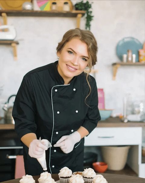 a woman is preparing cupcakes on a table in the kitchen with white frosting