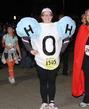 two women in costumes standing next to each other on the street at night with people walking behind them