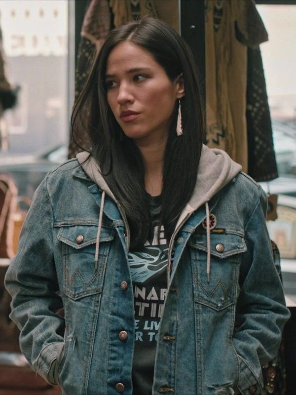 a woman standing in front of a store window with her hands in her pockets and looking at the camera