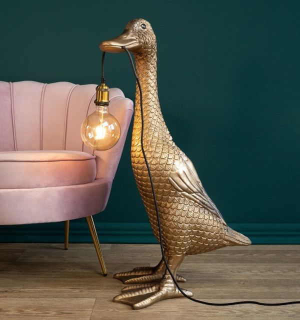 a gold duck lamp sitting on top of a wooden floor next to a pink chair