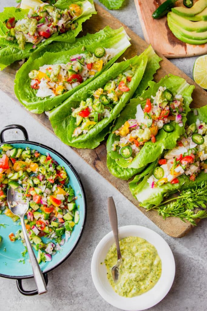 lettuce wraps with guacamole and salsa on a cutting board next to avocados