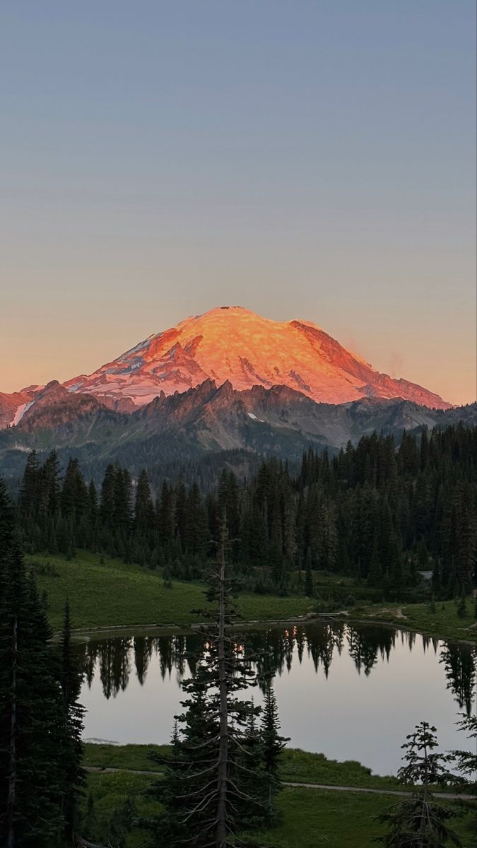 the sun is setting on a mountain with trees in front of it and a lake below