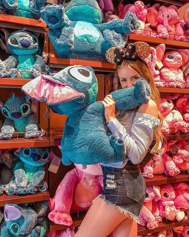 a girl is holding a stuffed animal in front of a store shelf full of stuffed animals