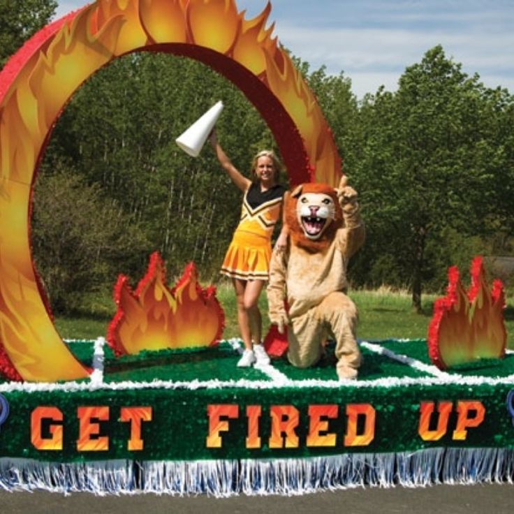 two people in costumes standing behind a float with fire and flames on it that says get fired up