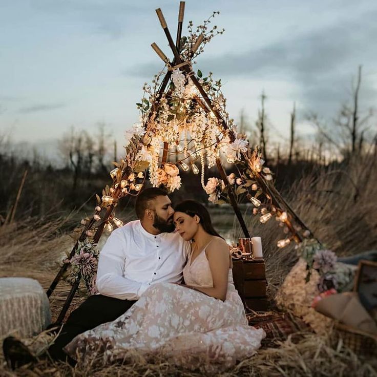 a man and woman are sitting in front of a teepee with lights on it