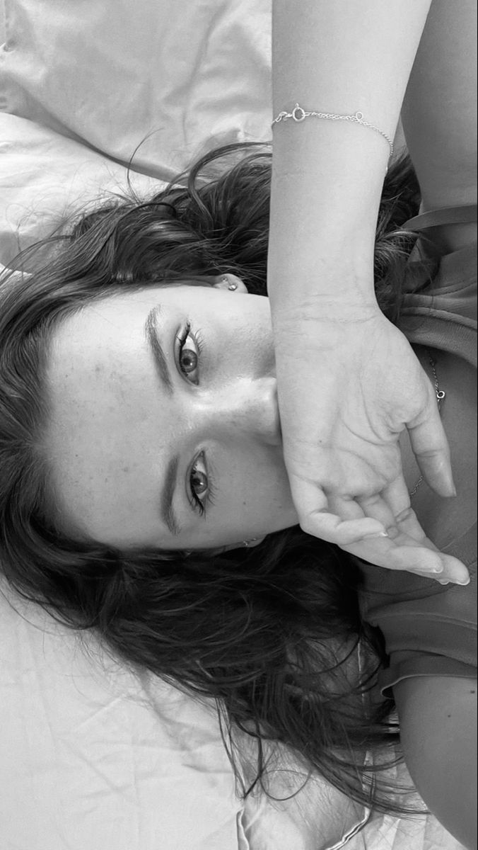 a black and white photo of a woman laying on a bed with her hand in the air