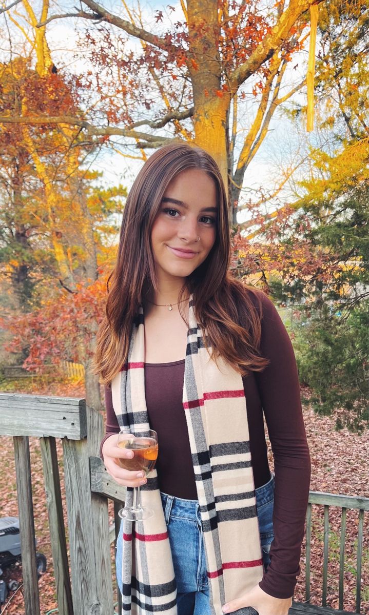 a woman standing on a deck holding a glass of wine and wearing a scarf over her shoulders