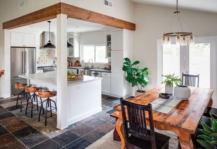 an open kitchen and dining room area with tile flooring, white walls, wooden beams, and wood accents